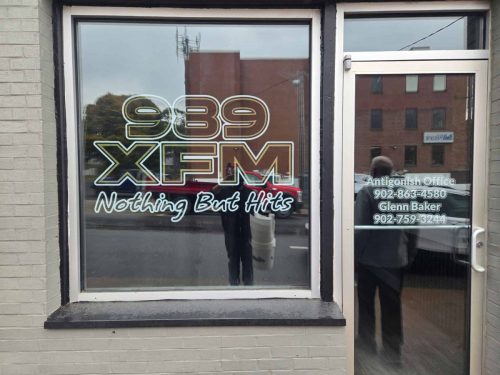 Front window and door of 989 XFM Antigonish office with custom vinyl lettering displaying the station’s logo, slogan “Nothing But Hits,” and contact information.