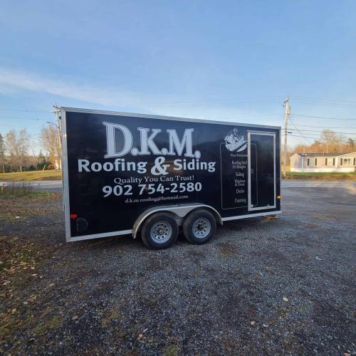 A trailer wrap for D.K.M. Roofing  Siding, featuring the business name, contact information, and list of services such as roofing, siding, windows, and decks, in bold black and white graphics.