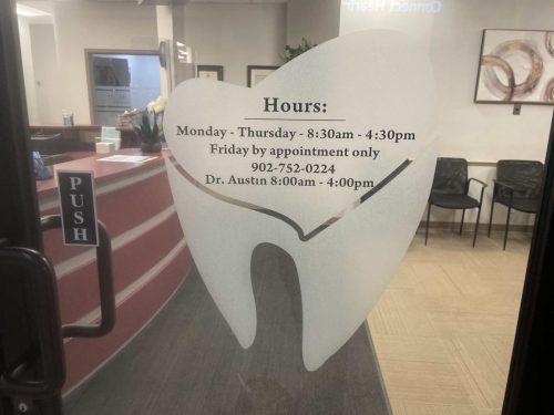 Dental office entrance door featuring frosted privacy film in the shape of a tooth with office hours and contact information.