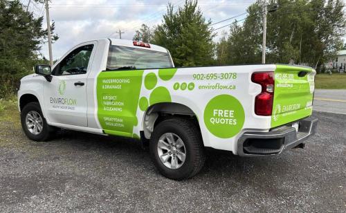 Side view of a white truck with a green and white wrap featuring the EnviroFlow logo and services such as waterproofing, air duct cleaning, and spray foam insulation. The truck also displays contact information and a 'Free Quotes' label on the rear side.