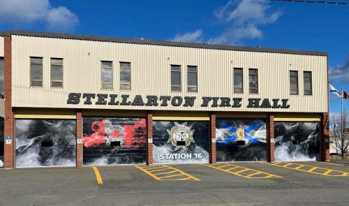 Front view of the Stellarton Fire Hall with newly wrapped bay doors featuring bold, smoke-inspired graphics. The doors showcase the Canadian flag on the left, Stellarton Fire Department emblem in the center, and the Nova Scotia flag on the right. The wrap design is sleek and impactful, adding a sense of pride and strength to the fire station’s exterior.