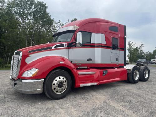 A red and silver semi-truck with a sleek vinyl wrap parked on a gravel lot, displaying the smooth and glossy finish of the wrap that looks like a fresh paint job.