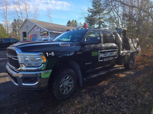 Black RAM 3500 with MacGregors Industrial decals parked in front of Auto Trim  Signs in New Glasgow, with the shop building visible in the background.