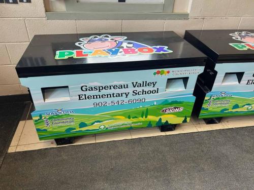 A colorful Play Box at Gaspereau Valley Elementary School with a bright landscape design, sponsor logos, and a playful PLAYBOX graphic on the lid.