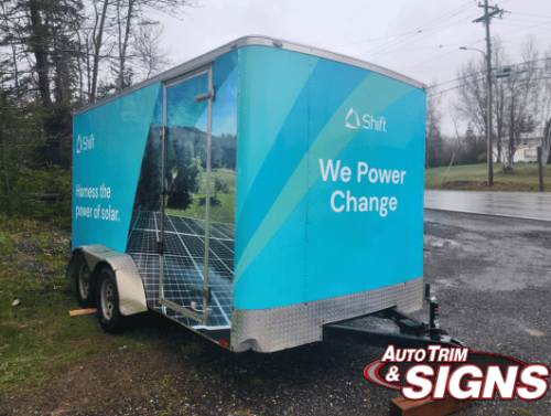 Side view of a trailer wrapped with Shift's branding in vibrant blue and white colors, featuring images of solar panels and the text 'We Power Change'