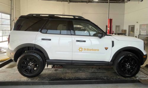 White Ford Bronco with St Barbara logo decal installed on the front door inside an automotive shop.