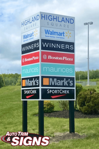 Tall multilayer signpost at Highland Square, displaying logos of various retailers including Walmart, Winners, Boston Pizza, Maurices, Mark's, and SportChek under a blue sky.