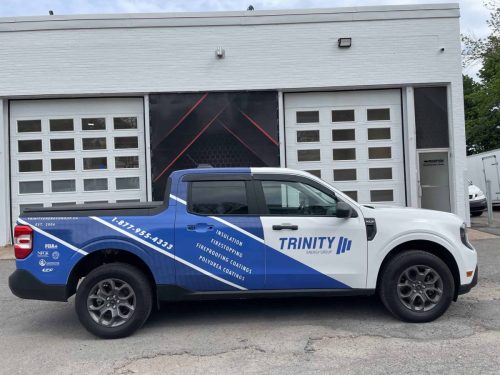 Side view of a Trinity Energy Group truck displaying custom vehicle graphics, service offerings, website, and contact information parked outside Auto Trim  Signs.