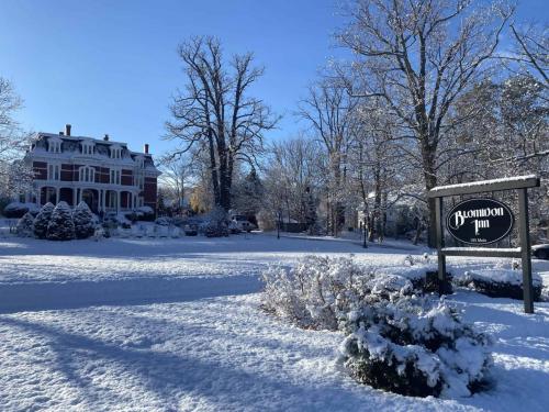 A picturesque winter view of the Blomidon Inn in Nova Scotia, surrounded by snow-covered trees and a bright blue sky. The iconic sign for the Blomidon Inn is in the foreground.