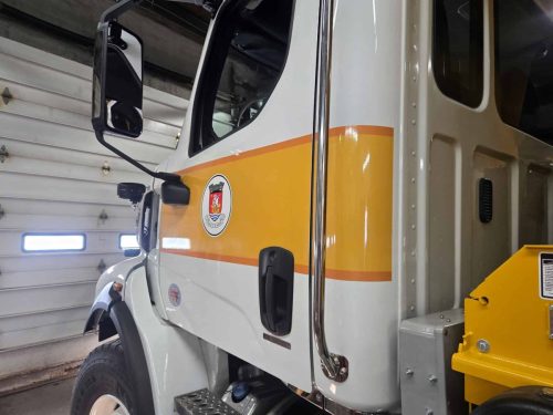 Close-up of municipal crest and striping on white truck cab.