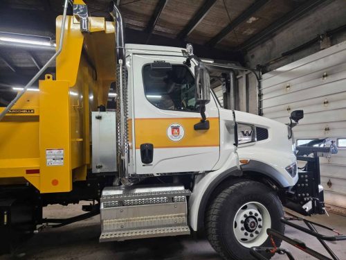 Full side view of yellow and white municipal dump truck inside garage.
