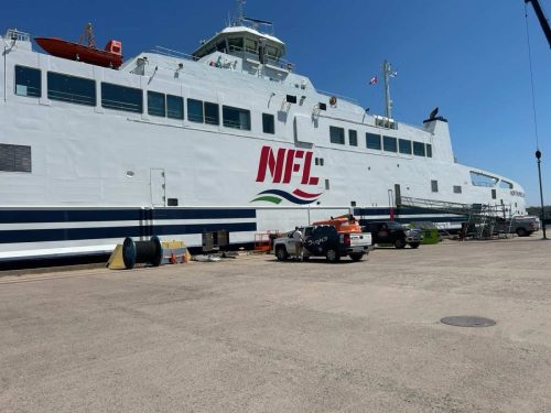 ferry docked at port, now featuring a bold new “NFL” logo and swoosh graphic applied by Auto Trim  Signs. Trucks and tools appear below the finished wrap.