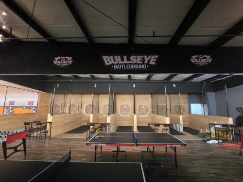 Indoor setup with multiple wooden axe throwing targets, ping pong table, and seating.
