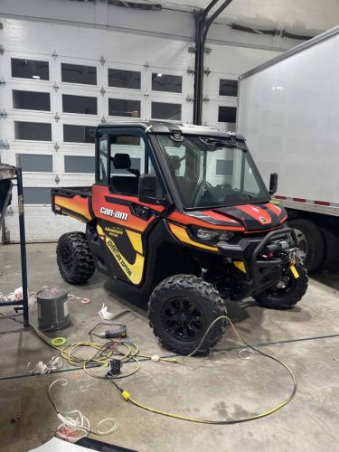 Angled front view of Can-Am side-by-side with custom black orange and yellow wrap installed