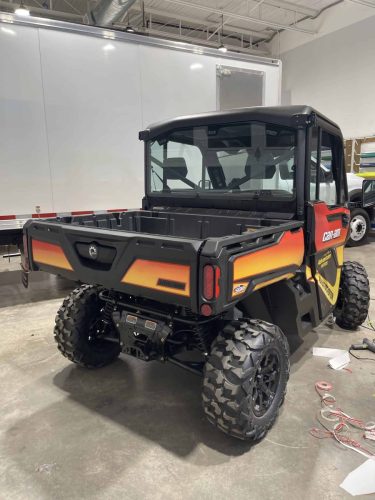 Rear side view of custom wrapped Can-Am side-by-side with orange and yellow Adventure Edition graphics