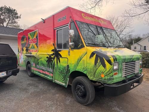 Side view of Caribbean Pot food truck featuring bold red, yellow, and green graphics with palm trees and a chef holding a dish.