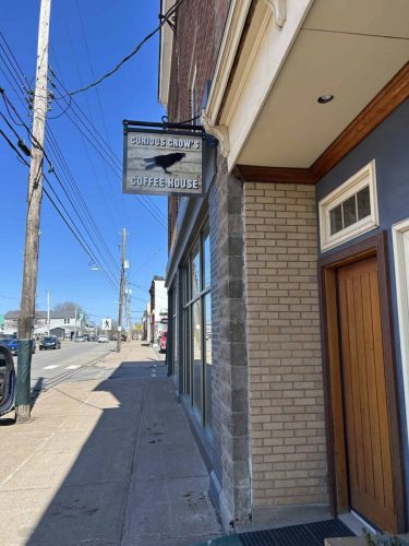 Hanging wooden sign for Curious Crow’s Coffee House on a downtown New Glasgow building exterior