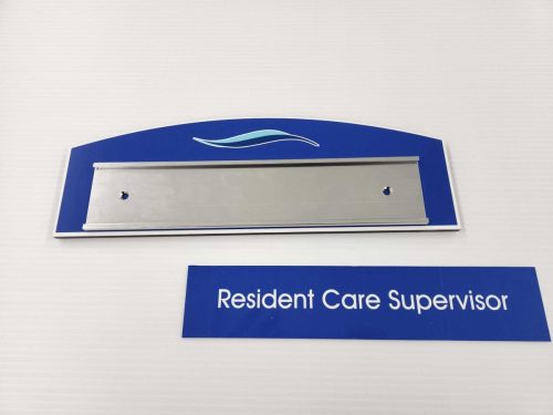 Custom CNC door sign with curved top and empty aluminum nameplate holder, displaying the loose nameplate ‘Resident Care Supervisor’ below.