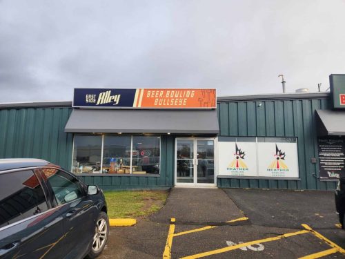 Exterior view of East Side Alley showing the installed storefront sign that reads “Beer. Bowling. Bullseye” along with branded window graphics for Heather Bowling Centres.