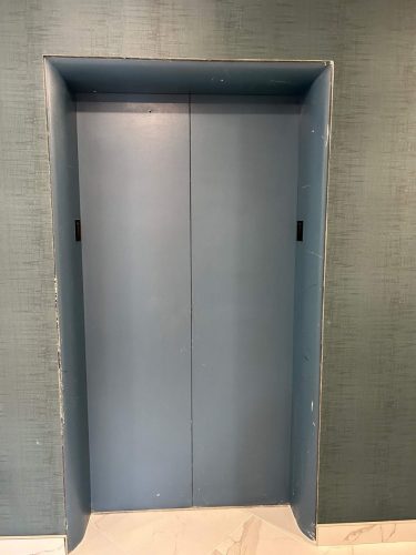 Grey elevator doors in a hallway before a vinyl wrap transformation.