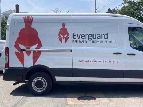 White Everguard Fire Safety van with red helmet logo, company branding, bilingual fire safety text, website, and phone number.