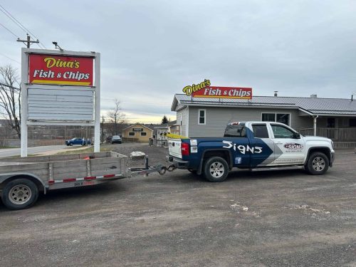 Auto Trim  Signs service truck parked in front of Dina’s Fish & Chips in Stellarton, with a newly installed rooftop sign and a roadside pylon sign both displaying the restaurant’s name in bold red and yellow branding.
