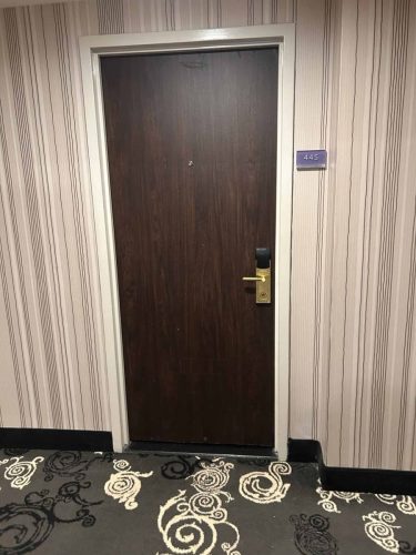 Worn dark wood hotel room door with visible damage before refinishing.