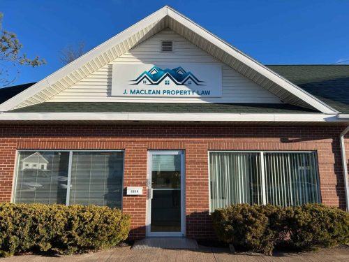 Exterior of J. MacLean Property Law showing a new building sign with a blue roofline logo mounted on the gable above the entrance.