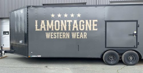 Dark grey enclosed trailer with large cream LaMontagne Western Wear lettering and five stars across the side.