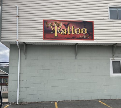 Side view of Last Stand Tattoo exterior wall sign mounted above parking area