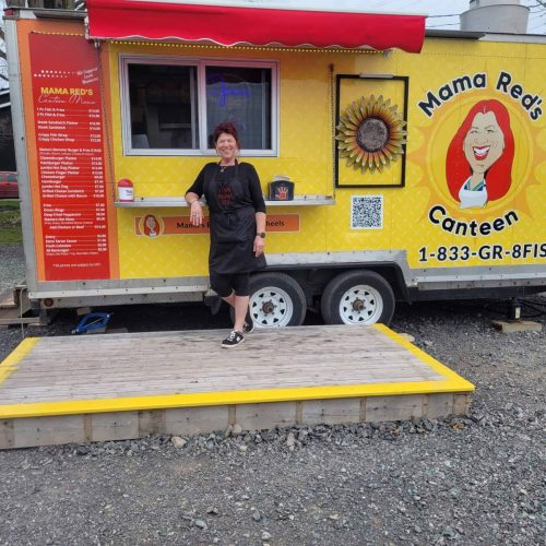 Mama Red standing proudly in front of her food truck, wearing a branded apron, with the serving window and business logo behind her.
