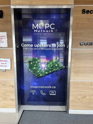 Custom elevator wrap for MOPC Network featuring a galaxy-style background, Nova Scotia network graphic, and promotional messaging installed on elevator doors inside a commercial building.