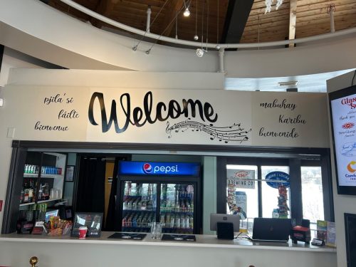 Custom welcome wall graphic at Glasgow Square Theatre featuring the word Welcome with musical notes and greetings in multiple languages above the concession area.