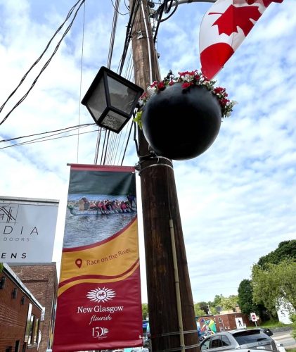 Decorative street banner featuring a dragon boat team and the text “Race on the River – New Glasgow Flourish” celebrating the town’s 150th anniversary.