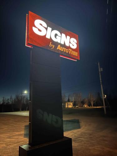 A tall, illuminated Auto Trim  Signs pylon sign glowing brightly at night against a dark sky. The bold red and white lettering stands out, casting a reflection on the ground.
