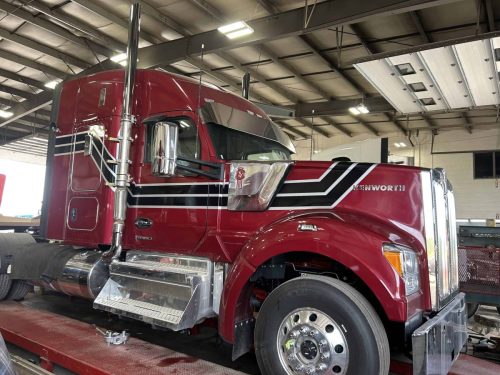 Red Kenworth semi truck with custom black and white striping installed along the cab and hood.
