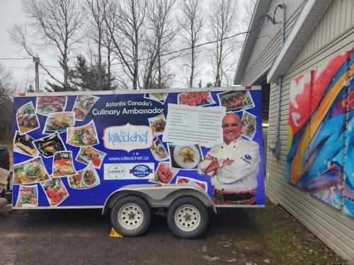 A bright and colorful trailer wrap for The Kilted Chef, featuring food photography, The Kilted Chef’s logo, and a recipe for Acadian Seafood Chowder.