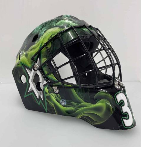 Side view of a custom-wrapped hockey goalie helmet displaying a swirling green smoke effect, a star-shaped logo, and the number 1 in bold white.