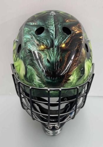 Front view of a custom-wrapped hockey goalie helmet with a detailed dragon design, including glowing yellow eyes and vibrant green and orange accents.