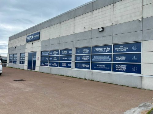 Exterior of Trinity Energy Group building with a full window wrap showcasing services and product categories in bold blue and white panels.