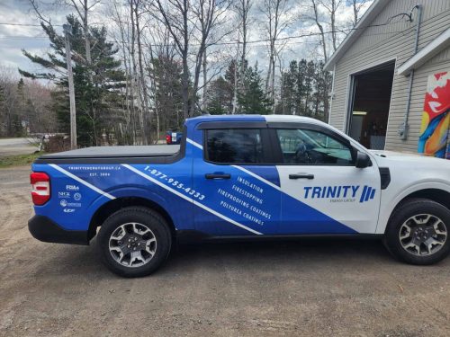 Side view of a Trinity Energy Group truck with a custom blue and white wrap showcasing services like insulation, firestopping, and coatings.