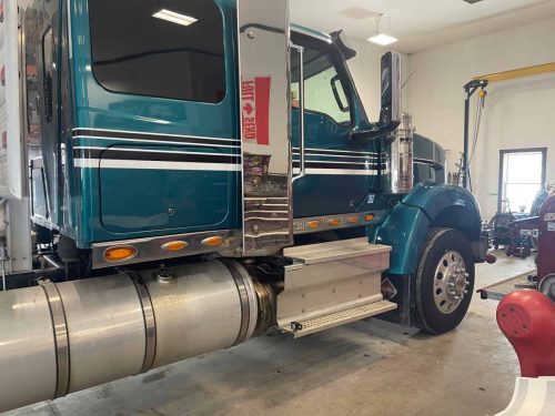 Teal semi truck cab with custom black and white striping installed by Auto Trim inside a shop.