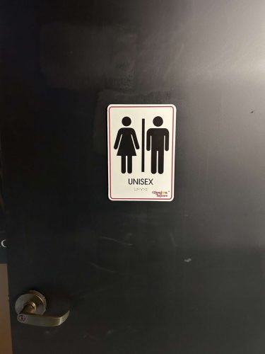 Unisex restroom sign mounted on a dark door inside a commercial space with braille