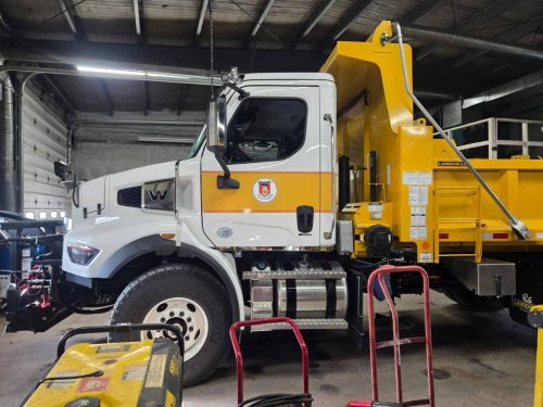 Yellow and white dump truck with municipal crest parked indoors.